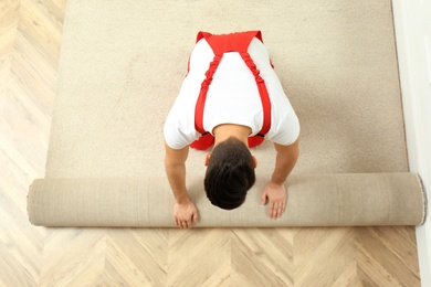 Photo of Worker rolling out new carpet flooring indoors, top view