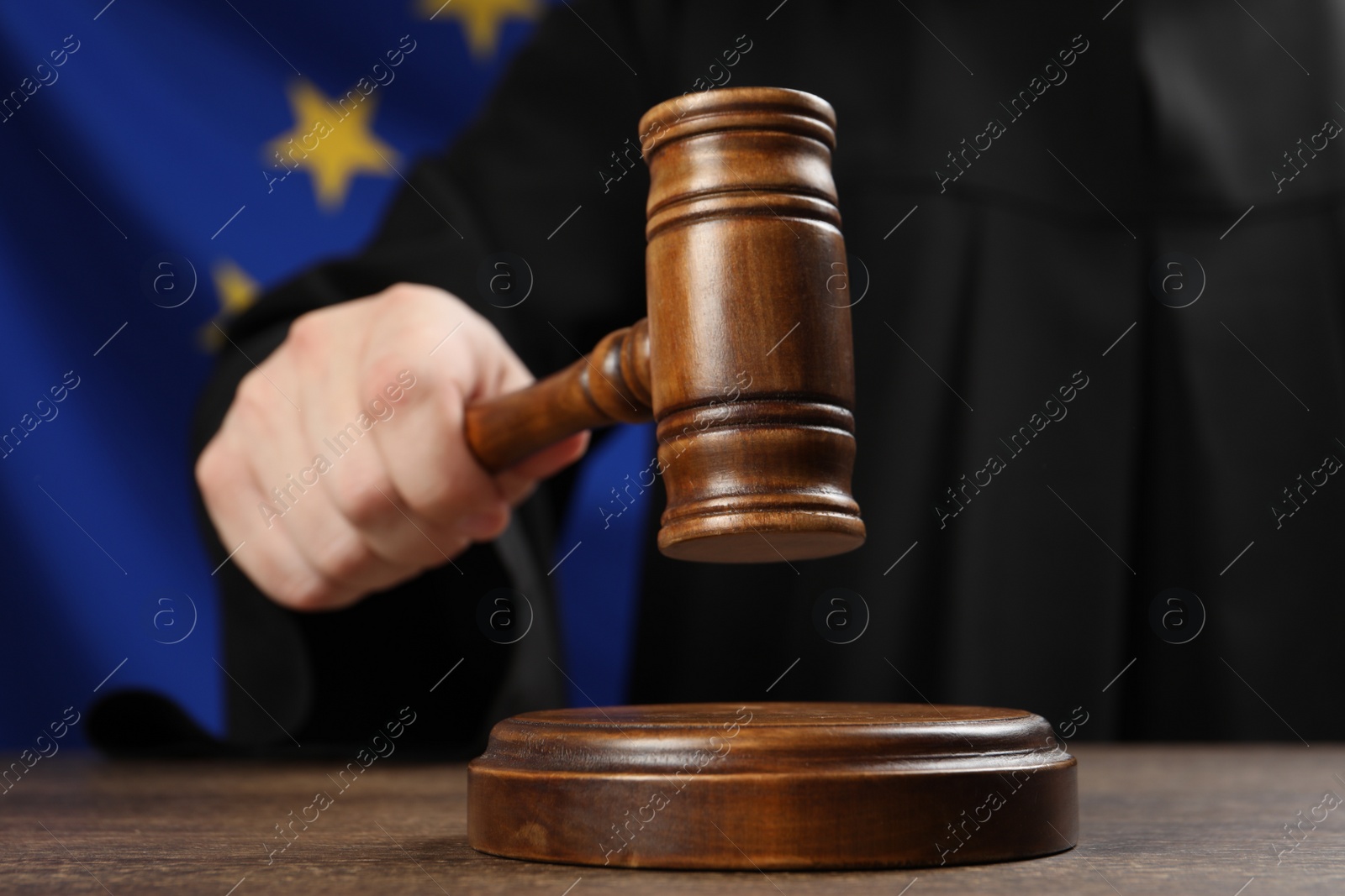 Photo of Judge with gavel at wooden table against flag of European Union, closeup