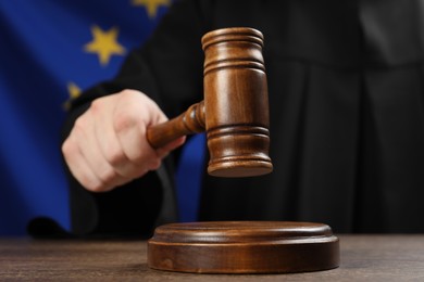Photo of Judge with gavel at wooden table against flag of European Union, closeup