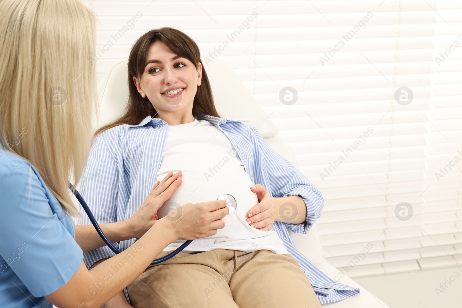 Photo of Pregnancy checkup. Doctor with stethoscope listening baby's heartbeat in patient's tummy in clinic. Space for text