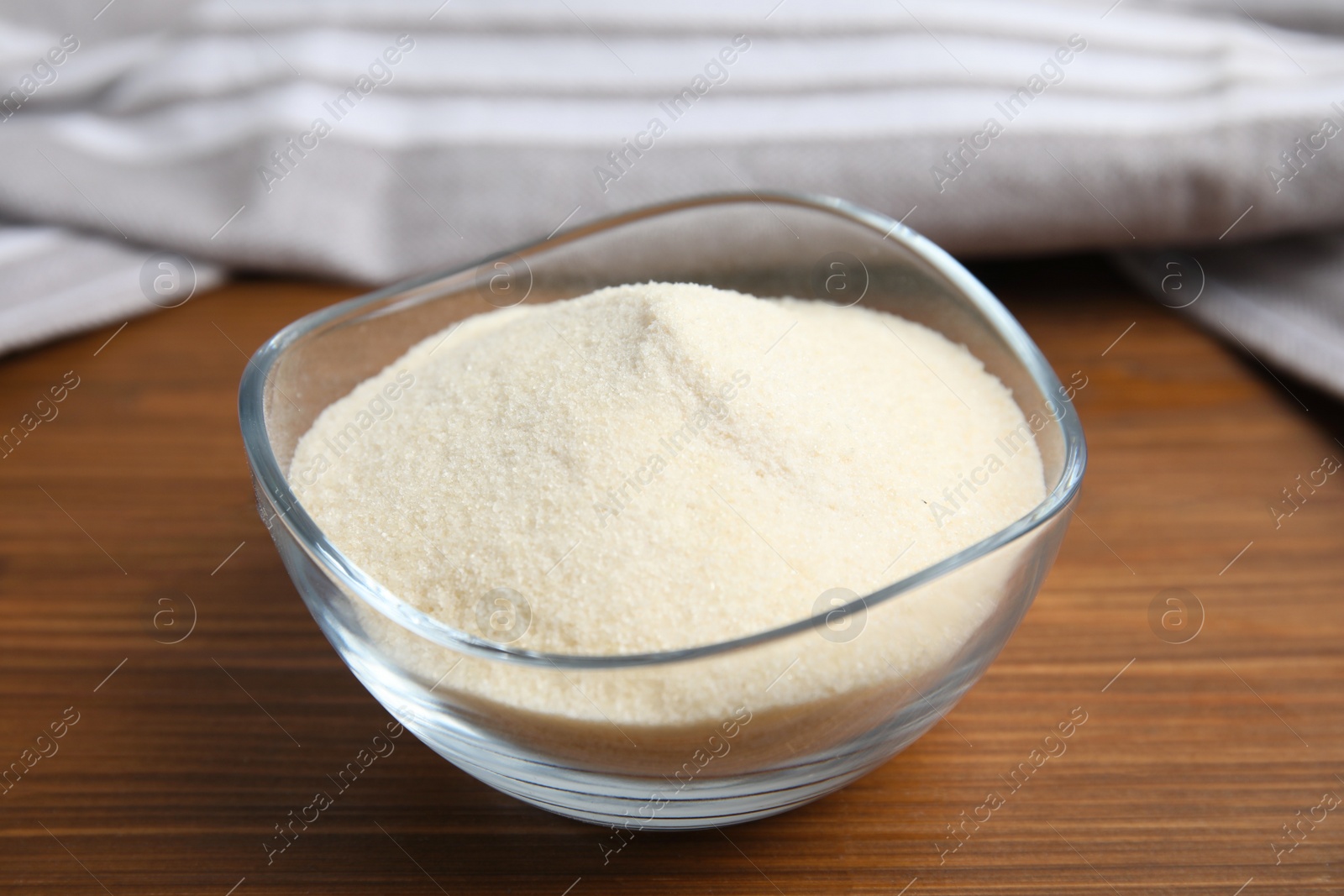 Photo of Gelatin powder in glass bowl on wooden table, closeup