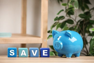Photo of Piggy bank and word SAVE made of colorful cubes on wooden table against blurred background