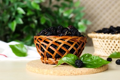 Wicker basket of delicious ripe black mulberries on white table