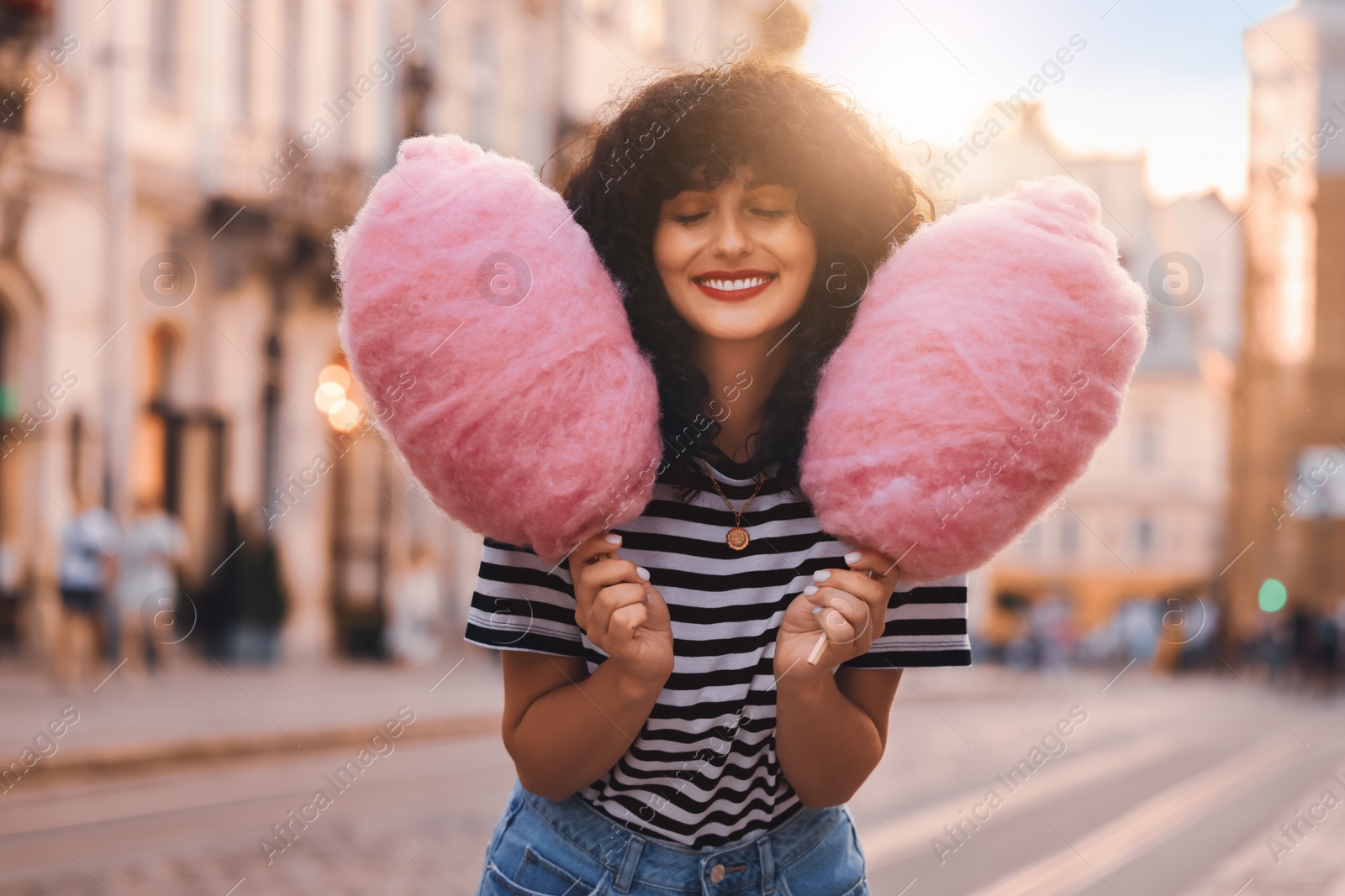Image of Portrait of happy woman with pink cotton candies in city on sunny day