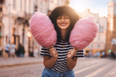 Portrait of happy woman with pink cotton candies in city on sunny day