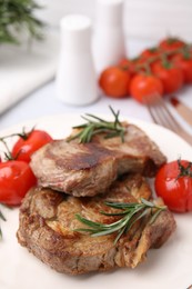 Delicious fried meat with rosemary and tomatoes on plate, closeup