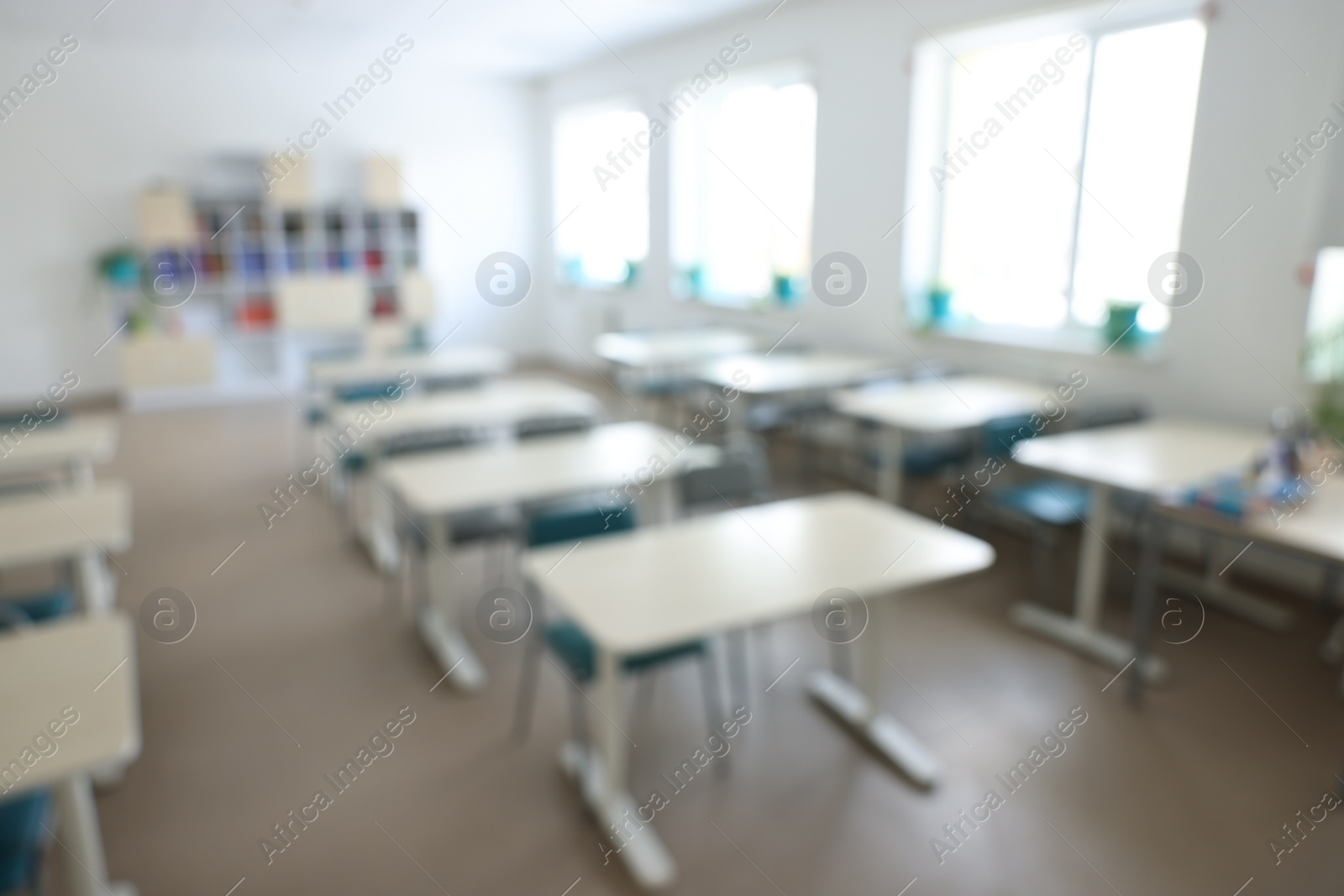 Photo of Blurred view of empty school classroom with desks, windows and chairs