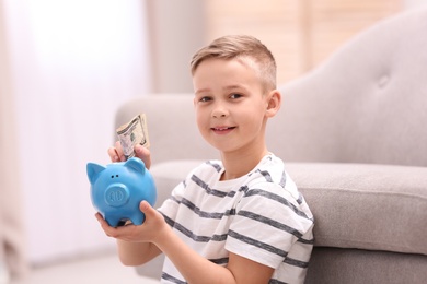 Photo of Little boy with piggy bank and money at home