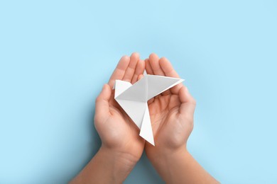 Photo of Origami art. Child holding paper bird on light blue background, top view