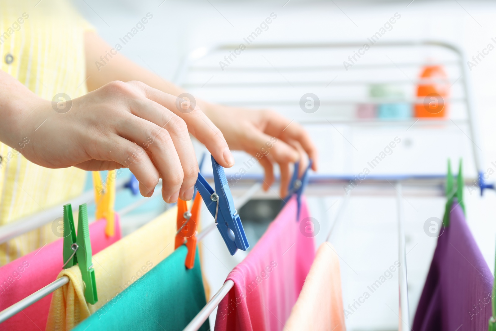 Photo of Woman hanging clean laundry on drying rack indoors, closeup