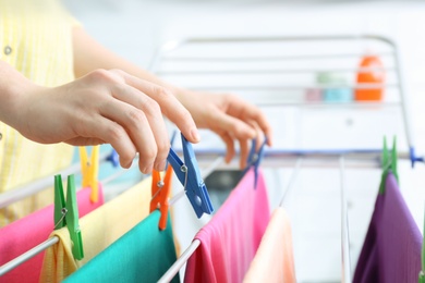 Woman hanging clean laundry on drying rack indoors, closeup