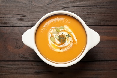 Photo of Tasty creamy pumpkin soup with dill and seeds in bowl on wooden table, top view