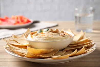 Photo of Delicious creamy hummus served with chips on wooden table