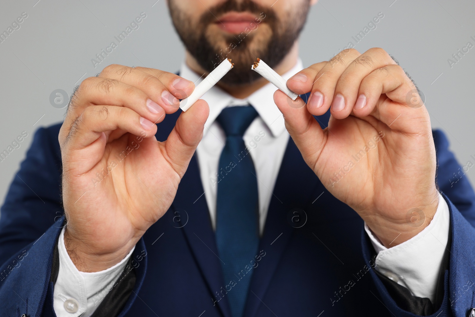 Photo of Stop smoking concept. Man breaking cigarette on light grey background, closeup