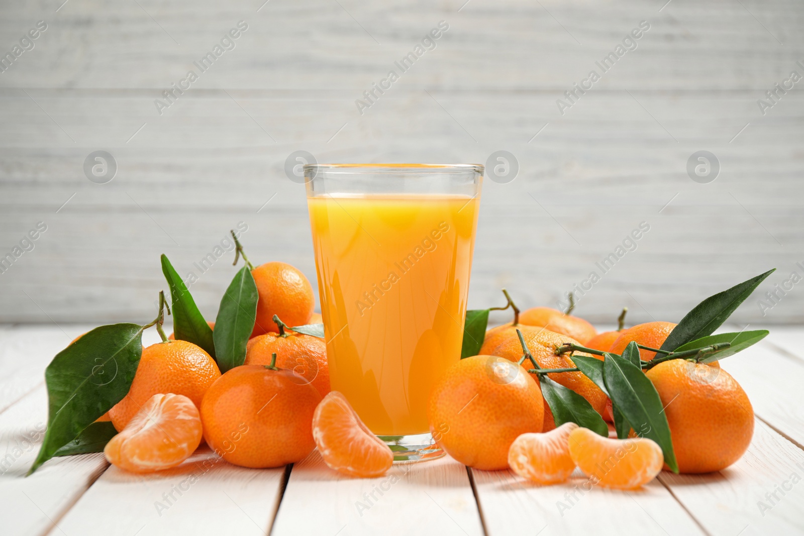 Photo of Glass of fresh tangerine juice and fruits on white wooden table