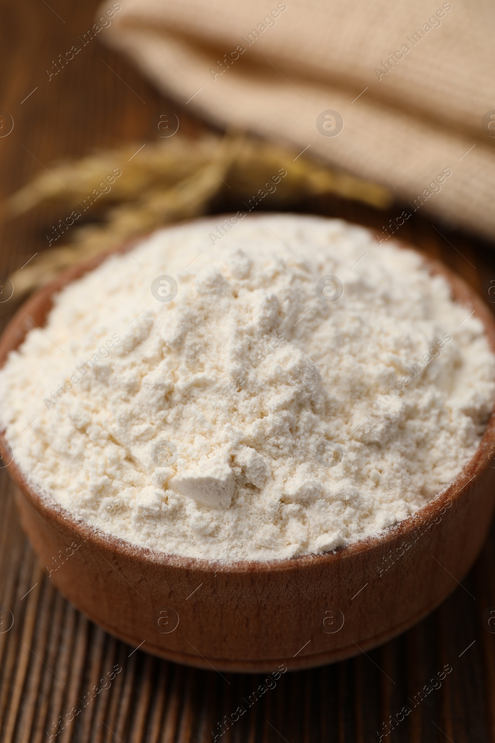 Photo of Bowl of organic wheat flour on wooden table, closeup