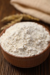 Photo of Bowl of organic wheat flour on wooden table, closeup