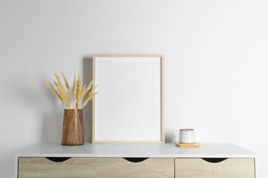 Photo of Empty photo frame, cup and vase with dry decorative spikes on white table. Mockup for design