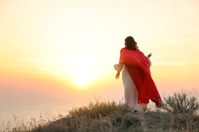 Photo of Jesus Christ on hills at sunset, back view. Space for text