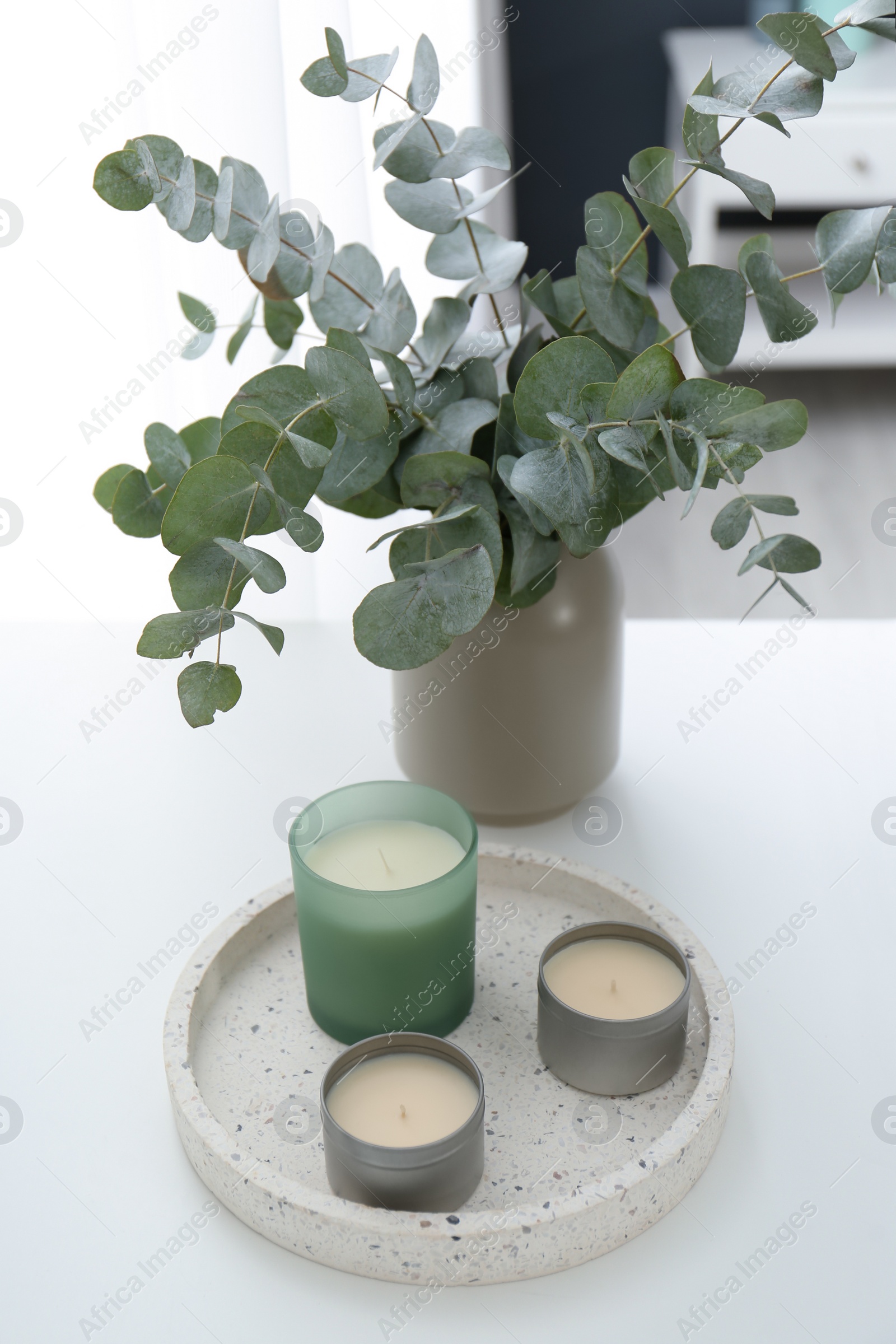 Photo of Candles and eucalyptus branches on white table indoors. Interior element