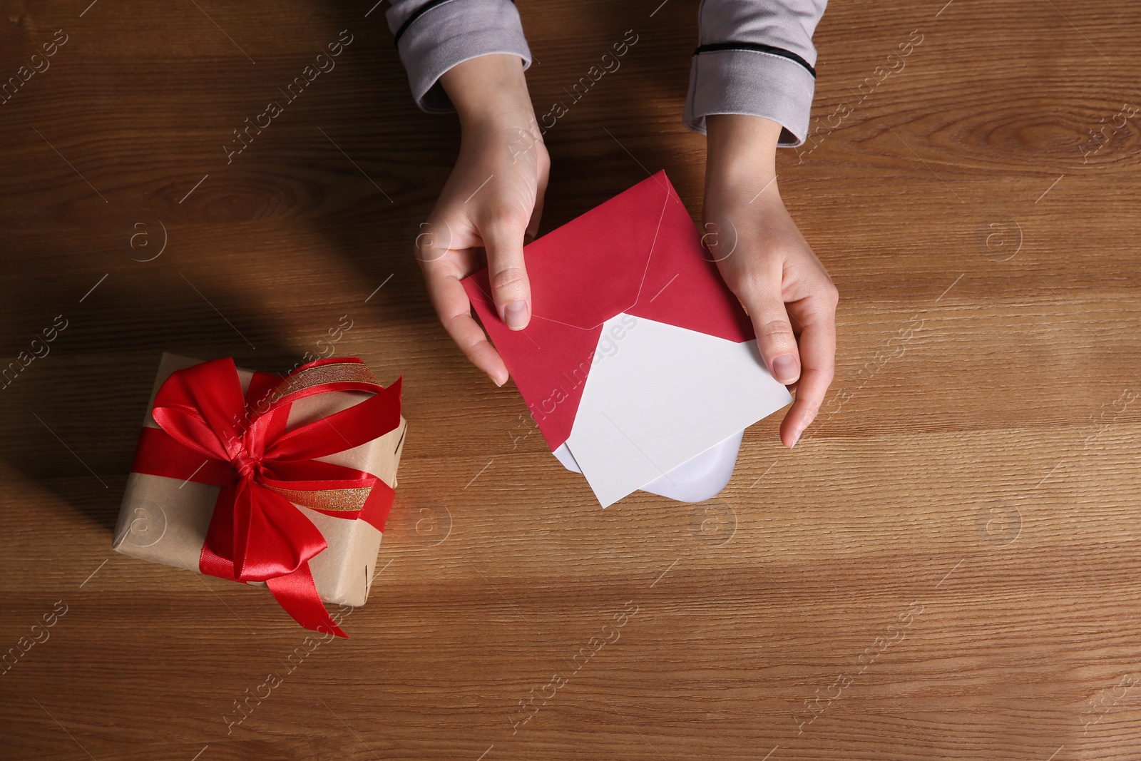 Photo of Woman holding envelope with blank greeting card and gift box on wooden table, top view