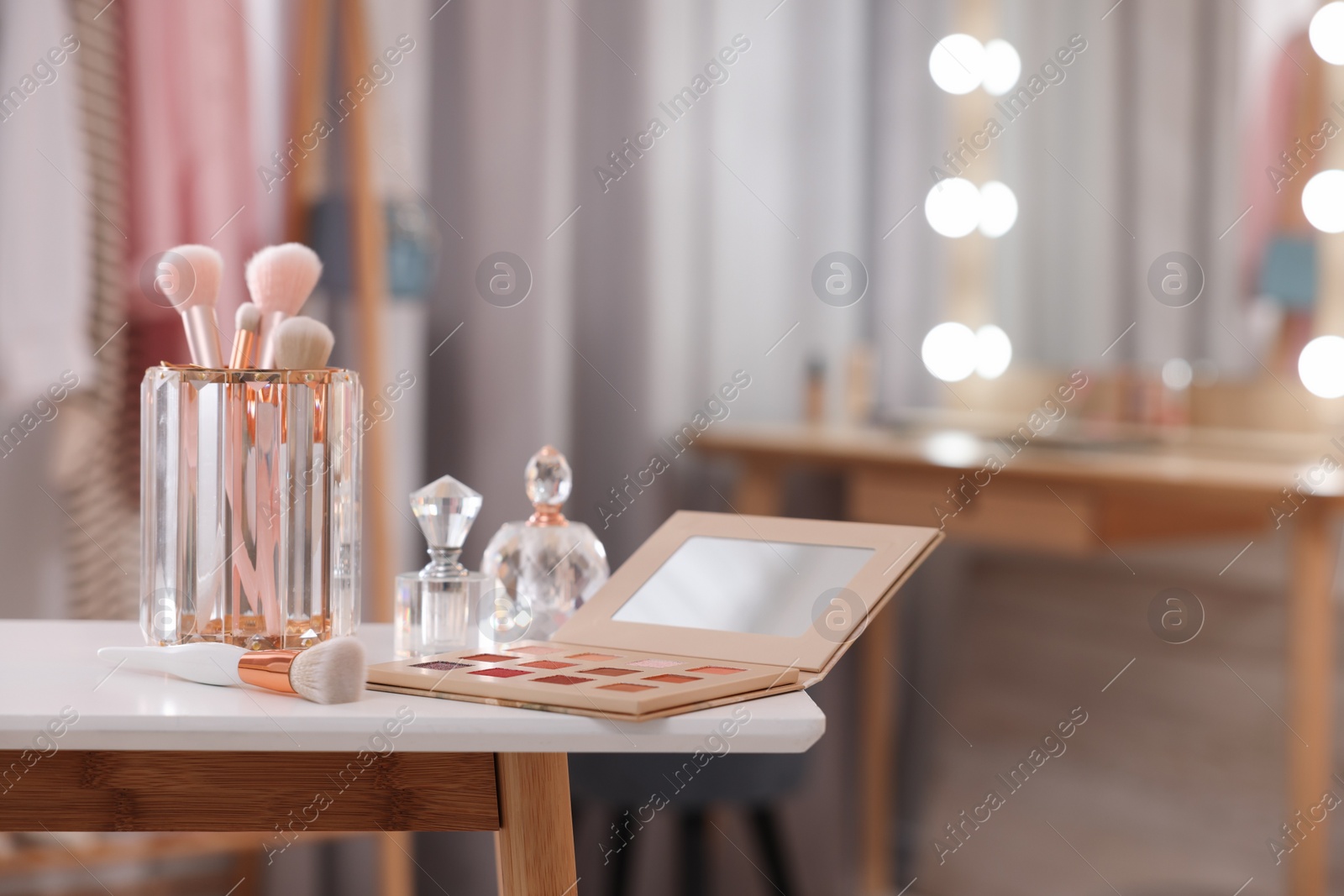 Photo of Set of brushes, eyeshadow palette and perfumes on white table in makeup room, space for text