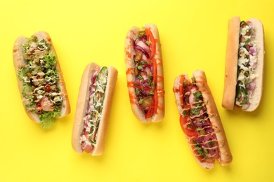 Photo of Delicious hot dogs with different toppings on yellow background, flat lay