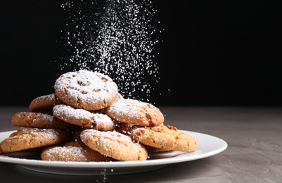 Photo of Woman with sieve sprinkling powdered sugar onto cookies at grey textured table, closeup