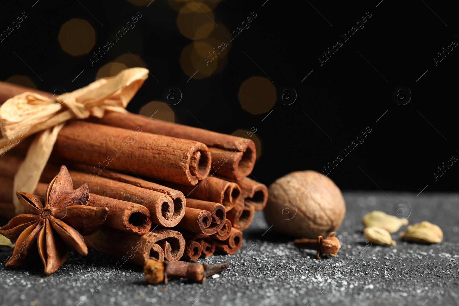 Photo of Different aromatic spices on grey textured table against black background, closeup. Space for text