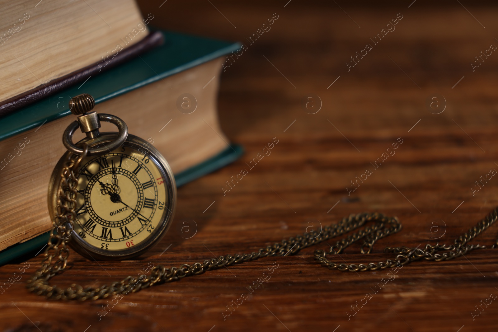 Photo of Pocket clock with chain and books on wooden table, closeup. Space for text