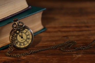 Pocket clock with chain and books on wooden table, closeup. Space for text