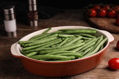 Photo of Raw green beans in baking dish on wooden table