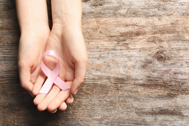 Photo of Woman holding pink ribbon on wooden background, top view. Cancer awareness