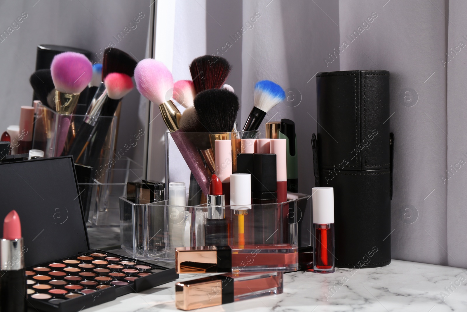 Photo of Bright lip glosses among different cosmetic products on white dressing table