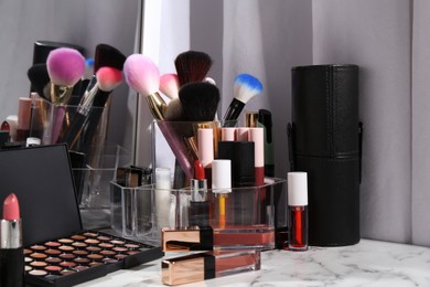 Bright lip glosses among different cosmetic products on white dressing table