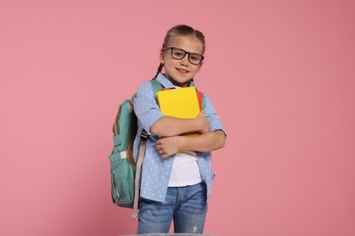 Photo of Happy schoolgirl in glasses with backpack and books on pink background