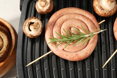 Electric grill with homemade sausage, rosemary and mushrooms on table, above view