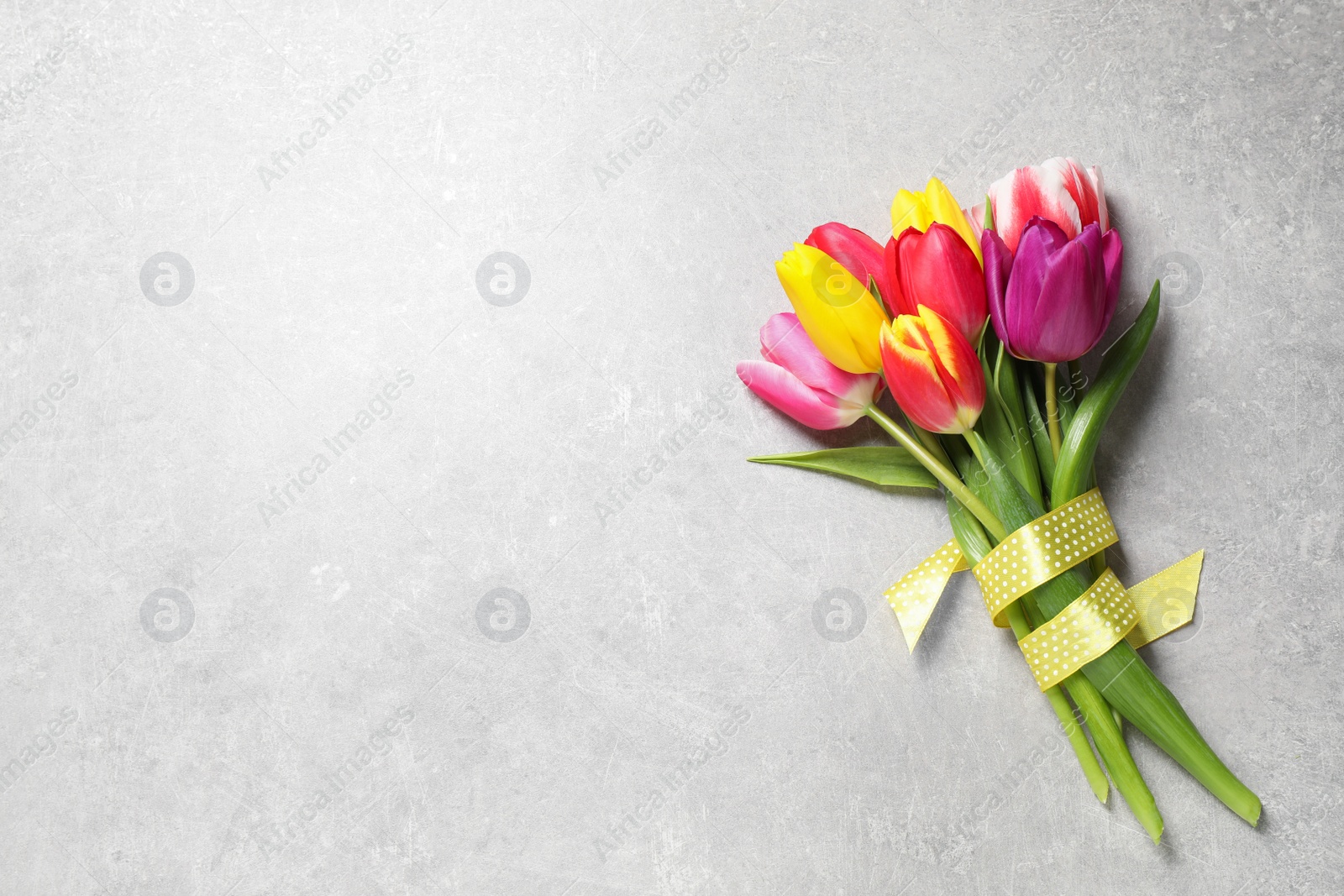 Photo of Beautiful spring tulips on light grey stone table, top view. Space for text