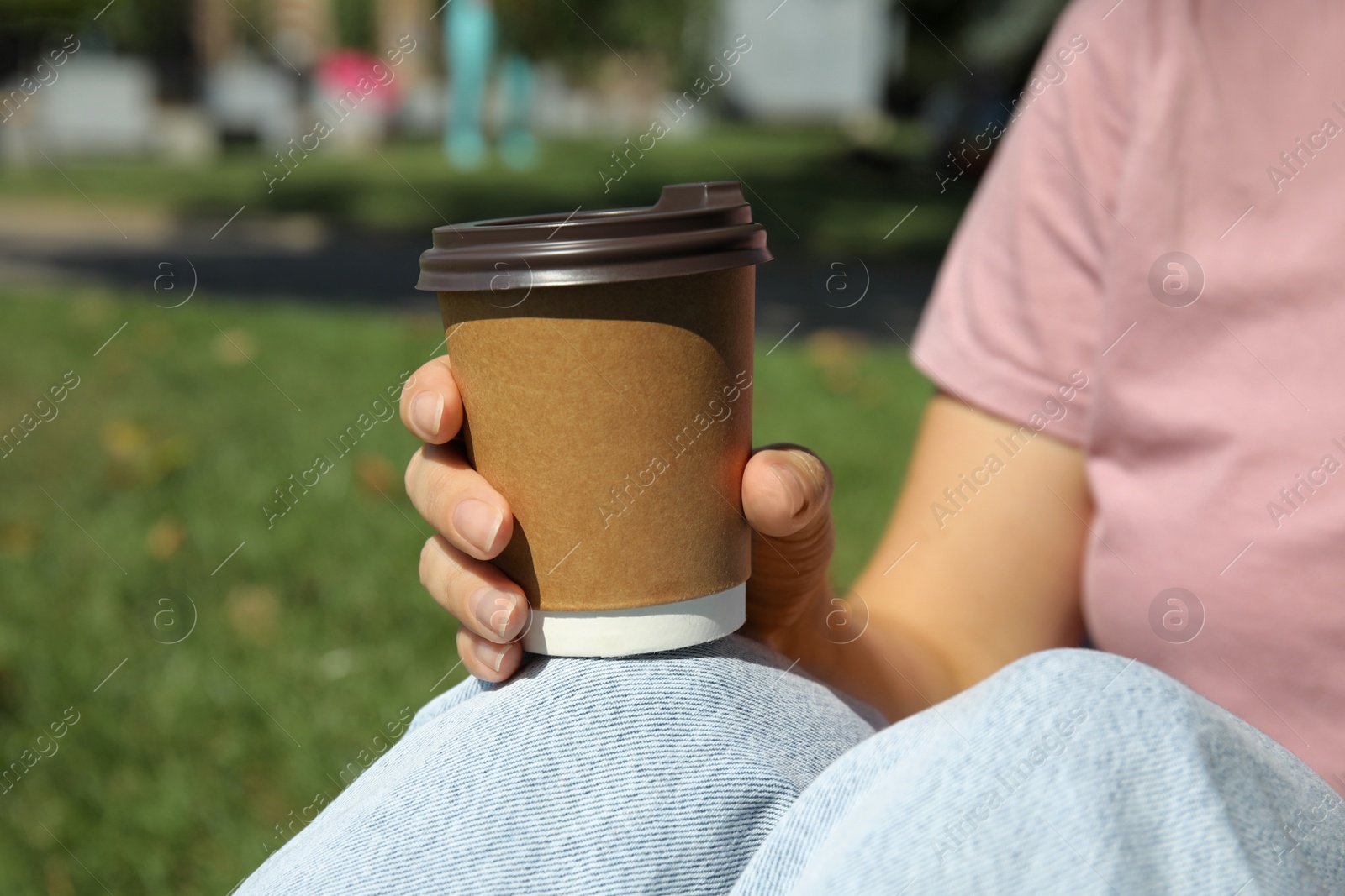 Photo of Woman holding takeaway cardboard coffee cup with plastic lid in park, closeup