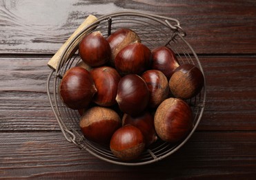 Photo of Sweet fresh edible chestnuts in metal basket on wooden table, top view