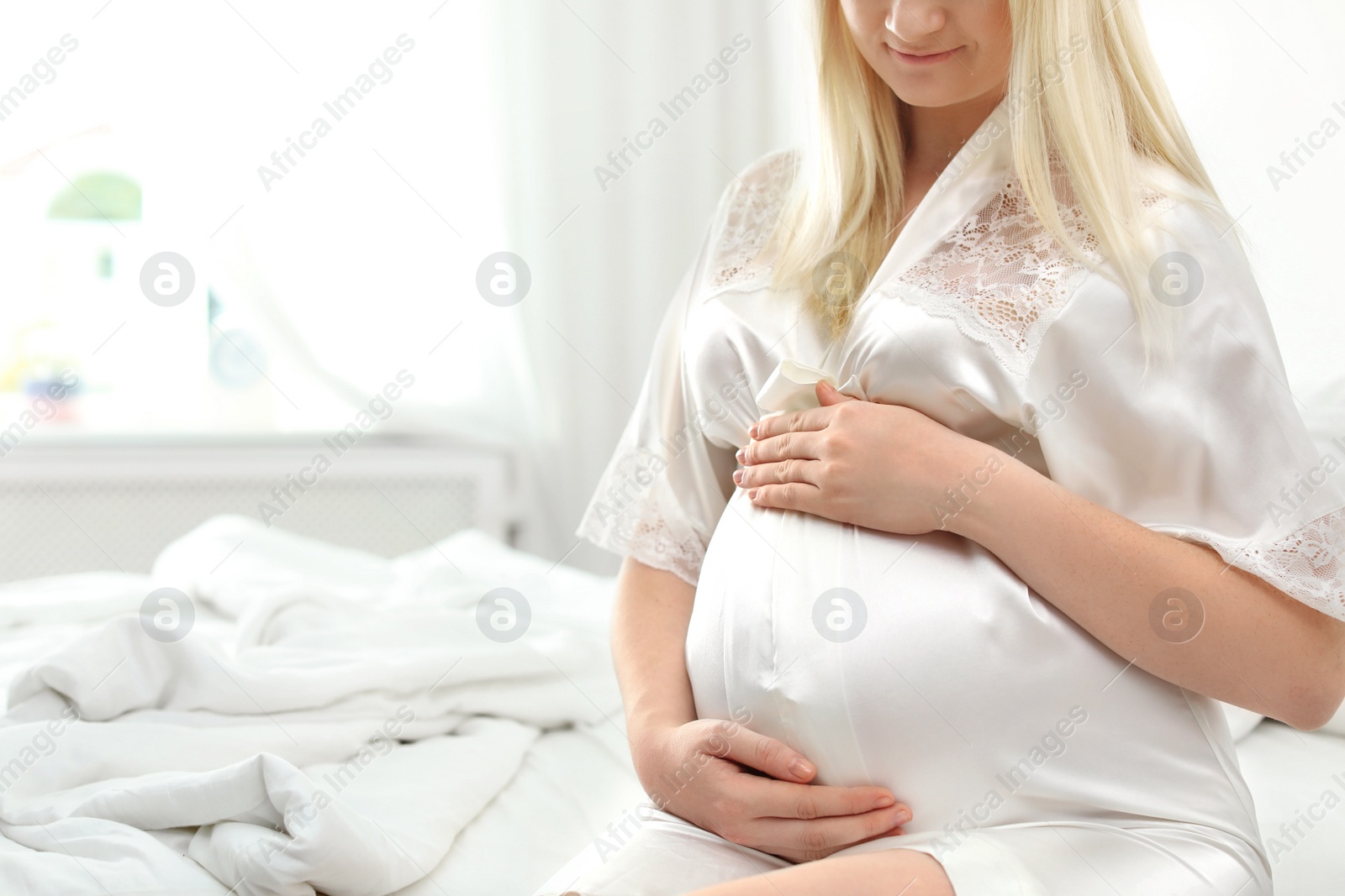 Photo of Pregnant woman sitting on bed in light room. Space for text