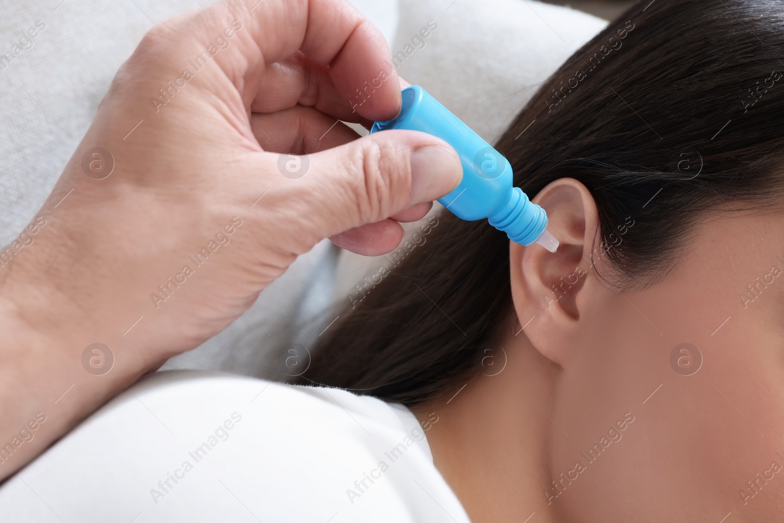 Photo of Senior man dripping medication into woman's ear on sofa, closeup