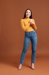 Photo of Young woman in stylish jeans on brown background