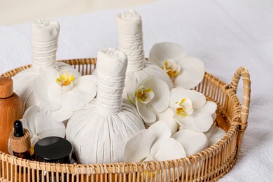 Photo of Wicker tray with herbal bags and different spa products on white bath towel, closeup