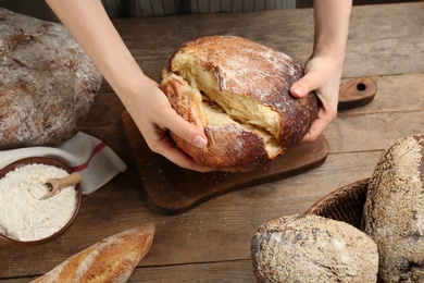 Photo of Woman breaking freshly baked bread at wooden table, closeup