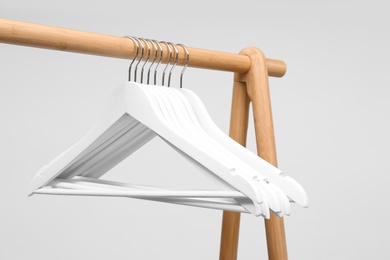 Photo of Empty clothes hangers on wooden rack against light background