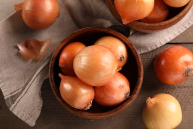 Many ripe onions on wooden table, flat lay