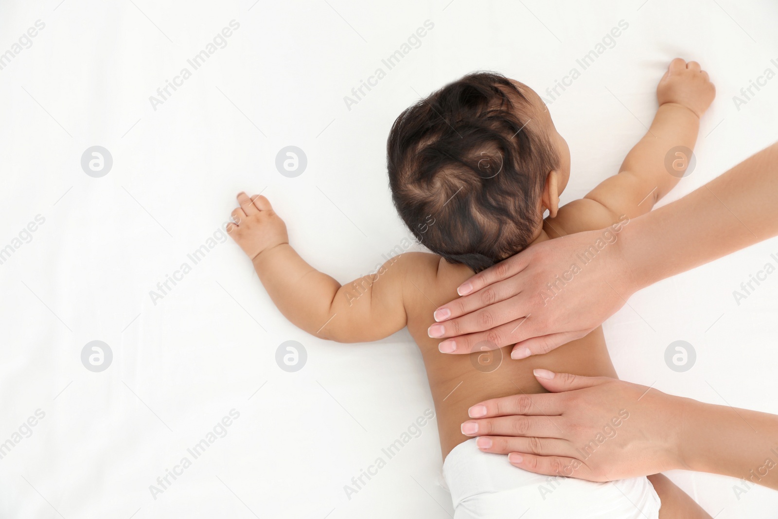 Photo of Top view of mother and her cute child on white bed, space for text. Baby massage and exercises