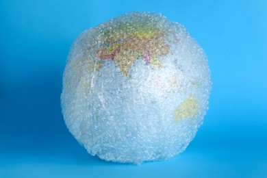 Photo of Globe packed in bubble wrap on turquoise background. Environmental conservation
