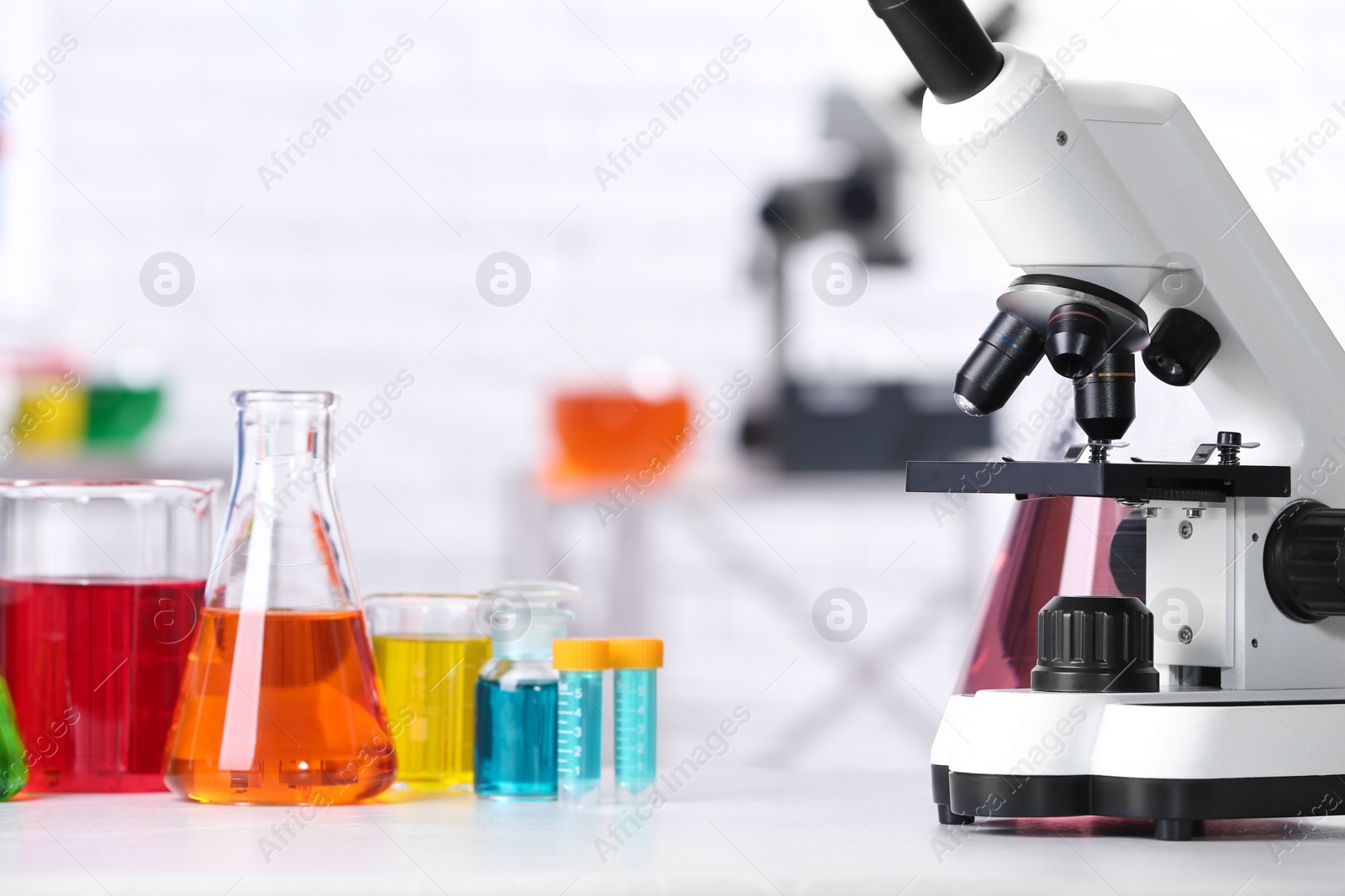 Photo of Different glassware with samples and microscope on table in chemistry laboratory